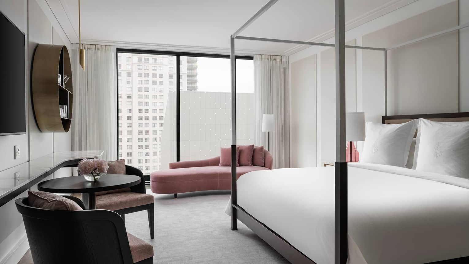 Hotel room with modern four-poster king bed, pink chaise and window