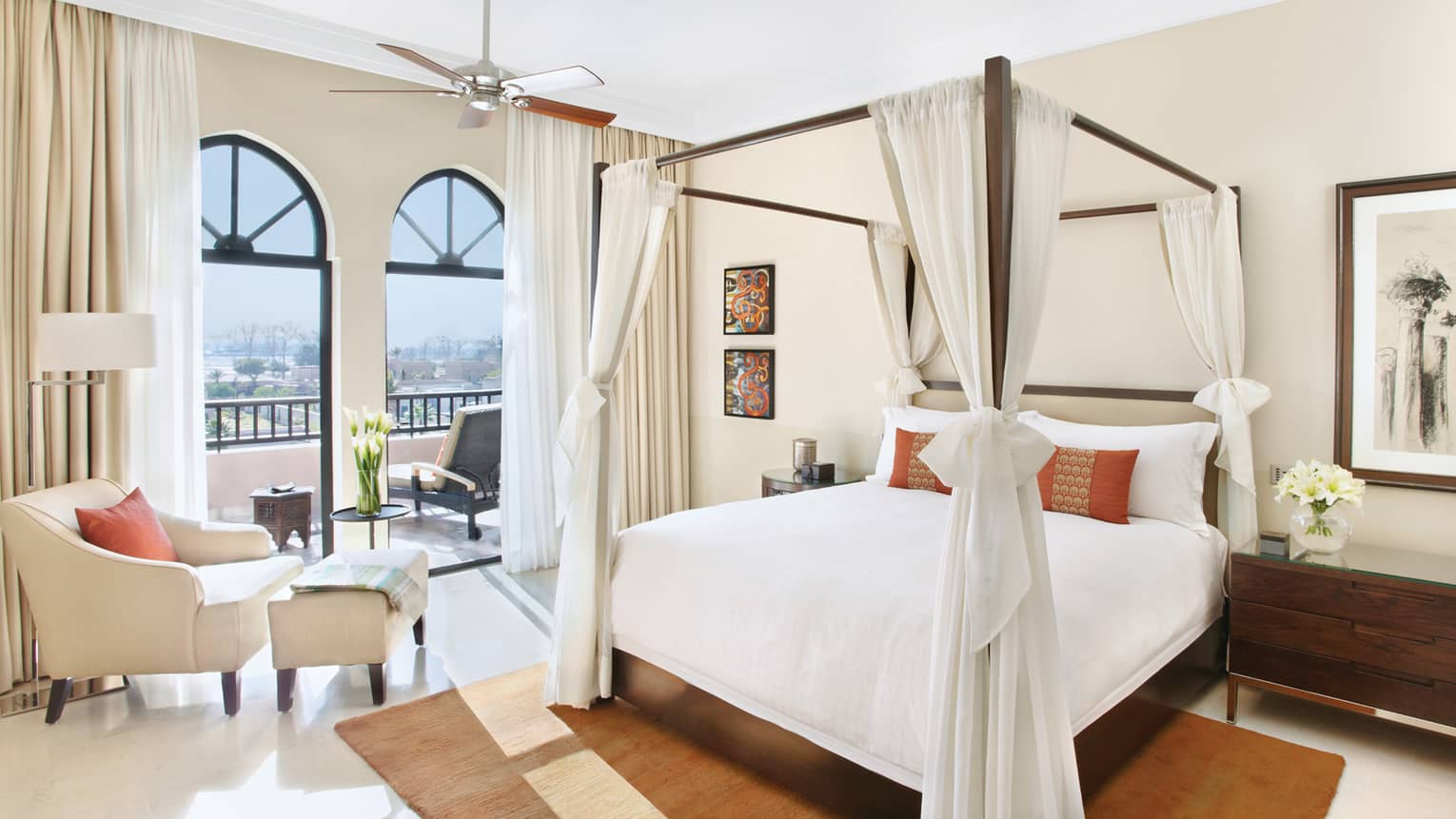 Panoramic Two-Bedroom Presidential Suite poster bed draped with white linens, armchair and footstool in front of sunny balcony windows