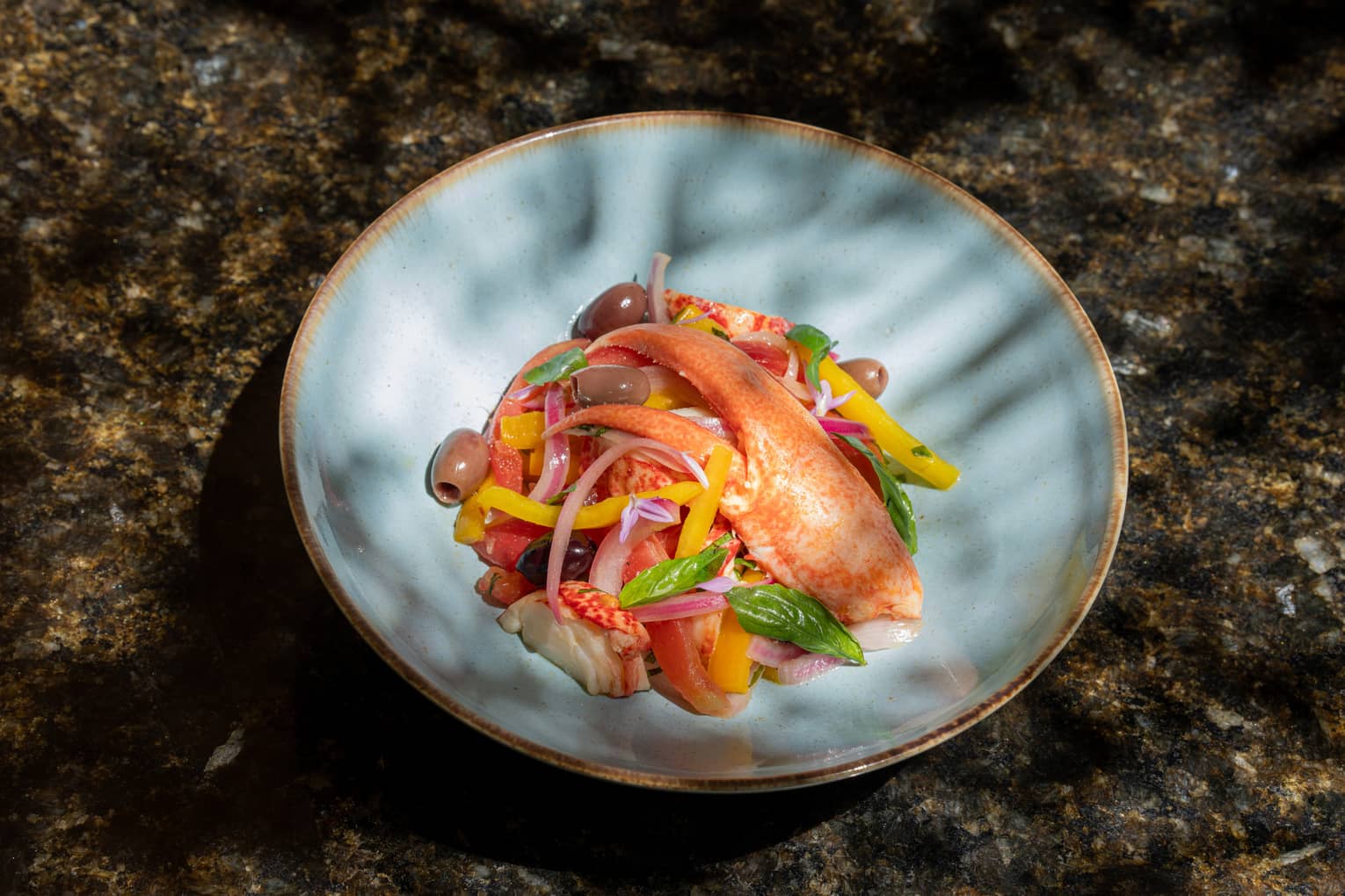 Octopus, lobster claw, olives and sliced onion in blue ceramic bowl