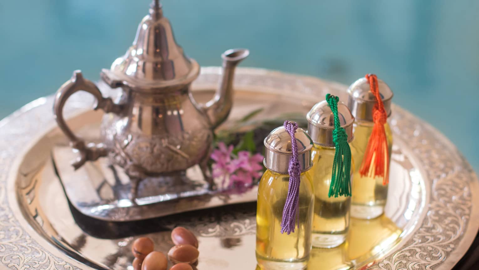 Silver teapot on platter with three glass jars of oil