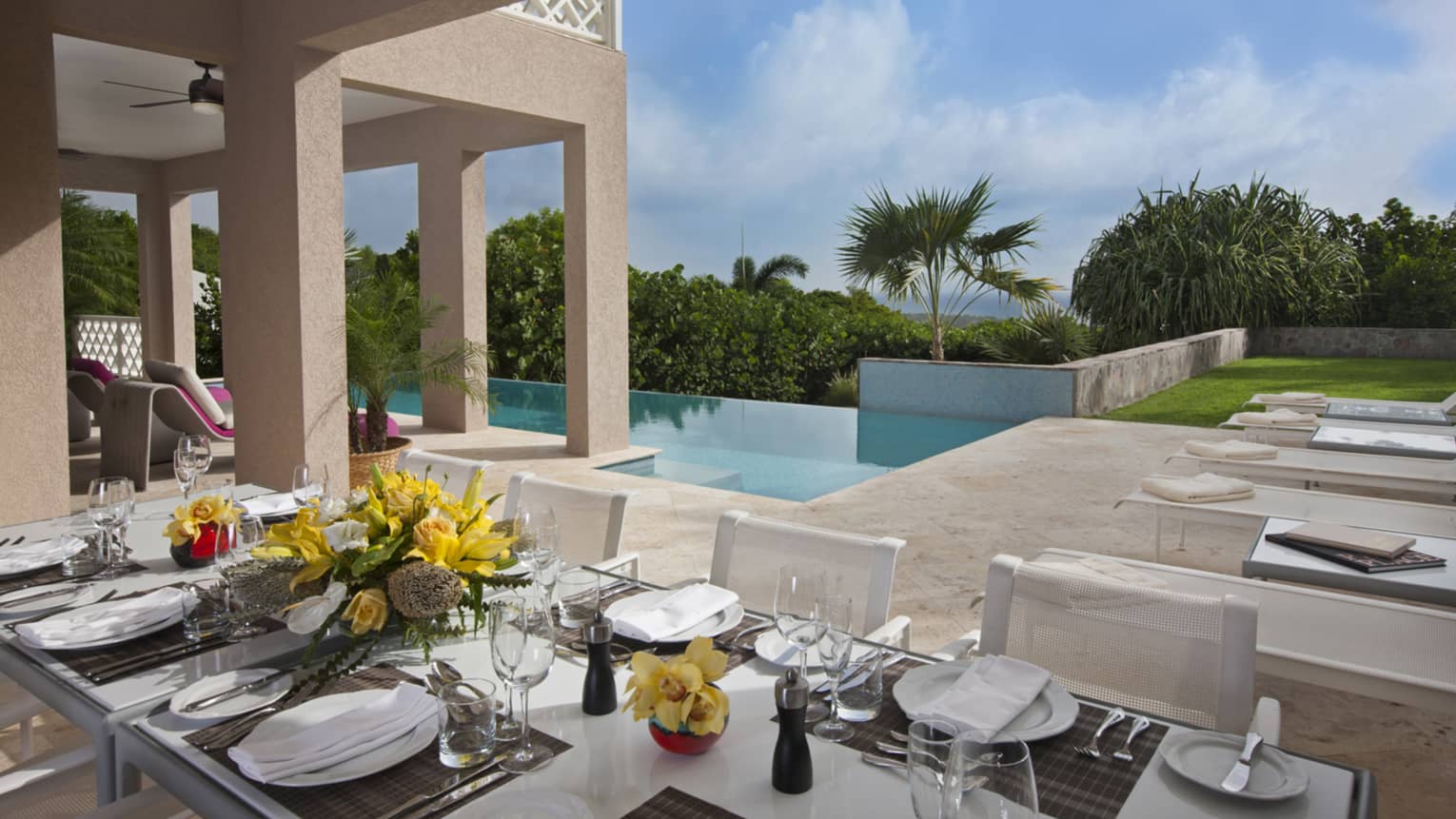 Formal dining table set with dishes, flowers on residence villa patio by pool