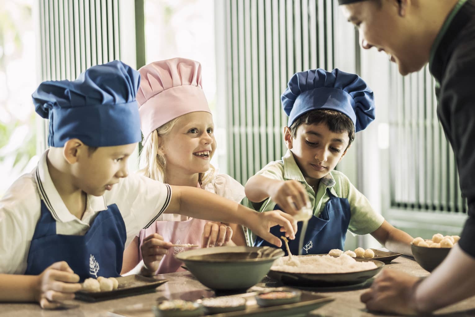 Three children with pink or blue chefs hats making food.