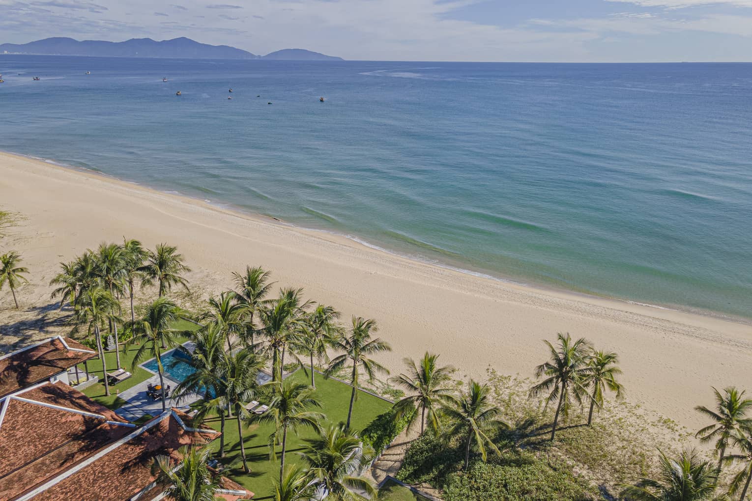 Three Bedroom Beachfront Pool Villa aerial shot with ocean and mountain views, palm trees and blue skies