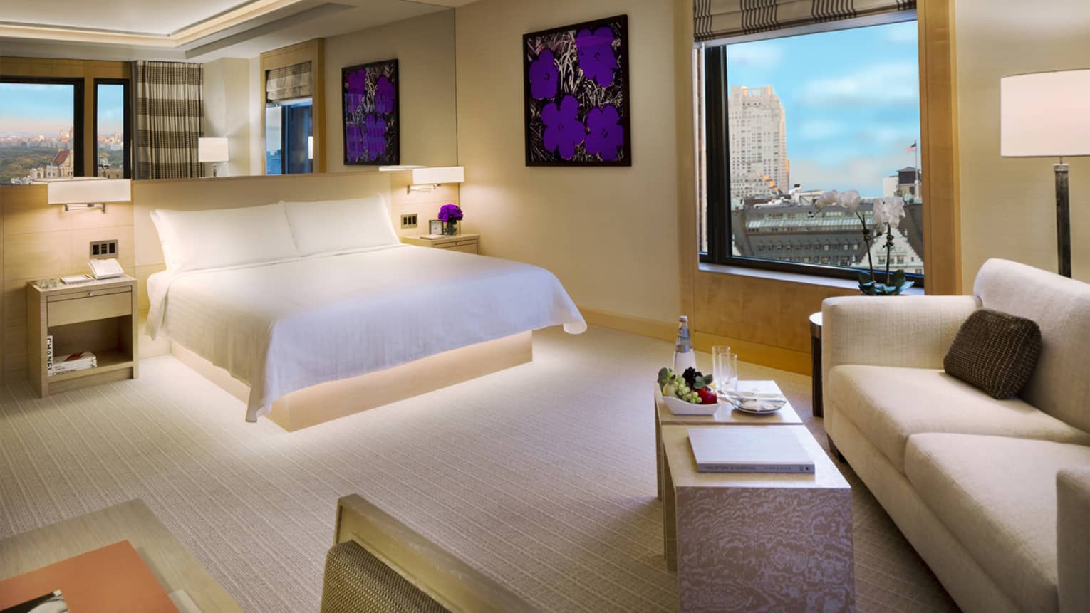 Modern Manhattan Junior Suite with framed purple flower print, white bed, sofa, window with park view