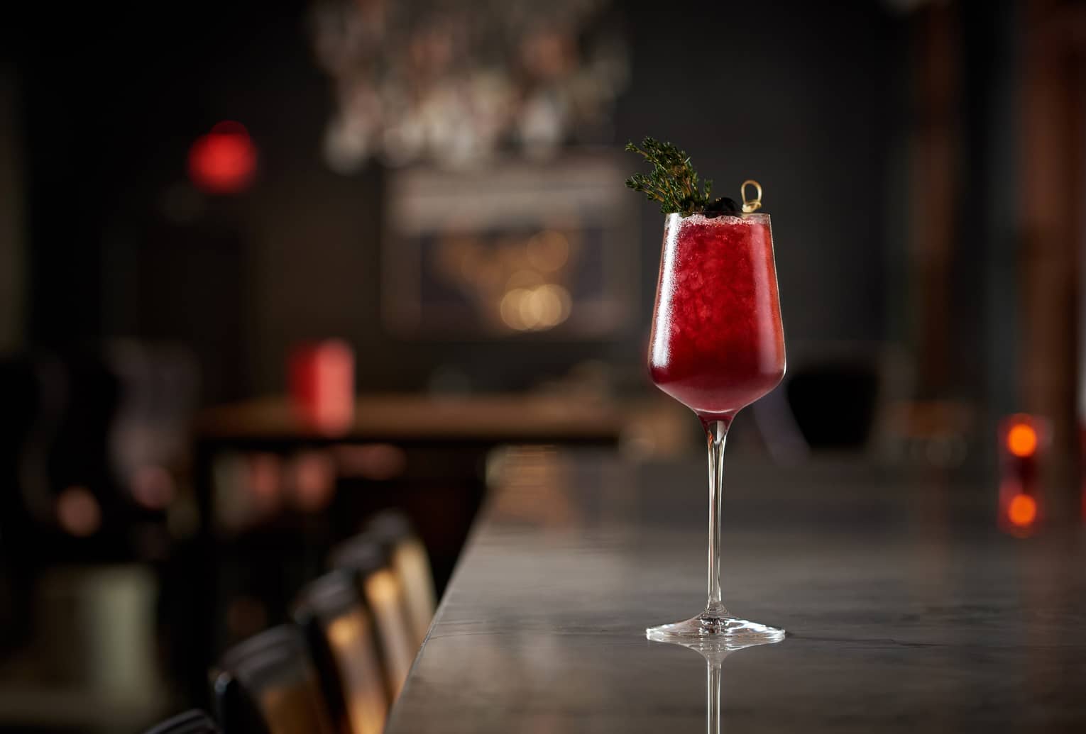 A red cocktail sitting on a dimly lit bar.