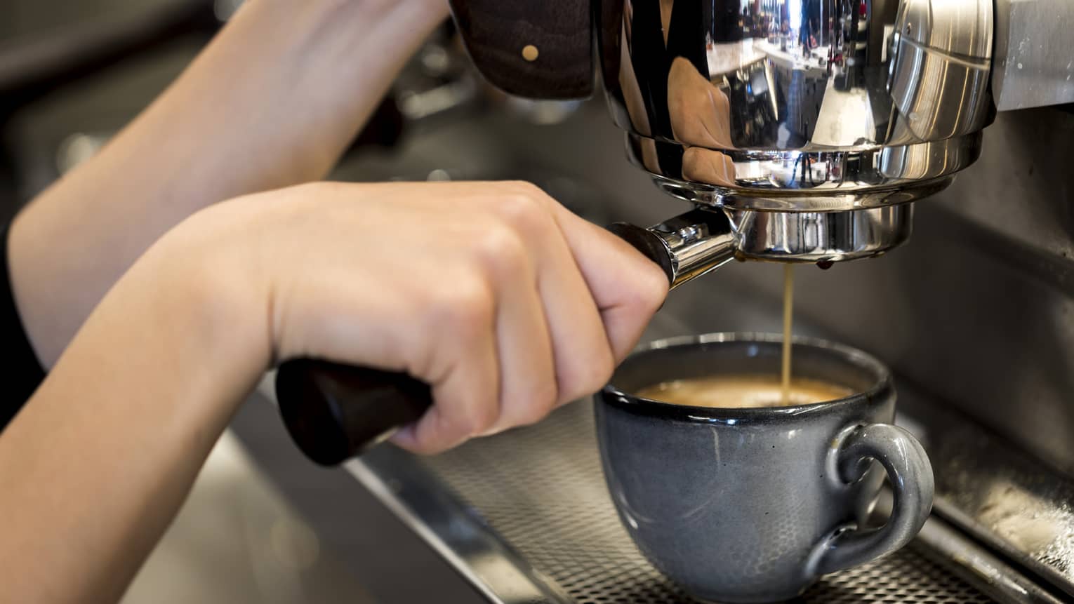 Close-up of hands pressing espresso in machine into small blue mug