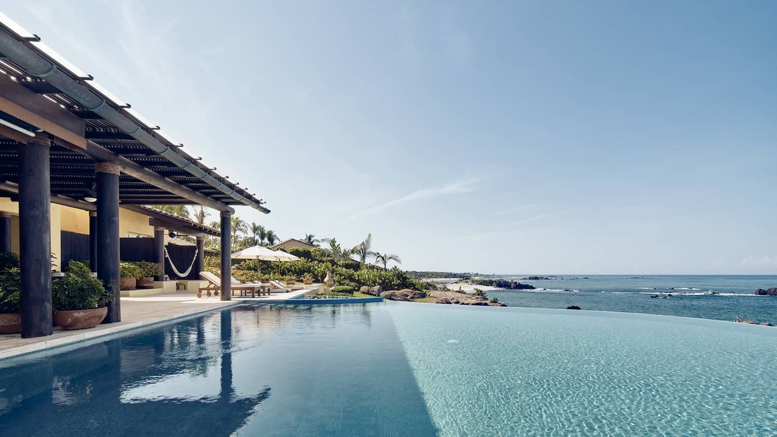 View over infinity swimming pool looking over ocean, covered patio at side