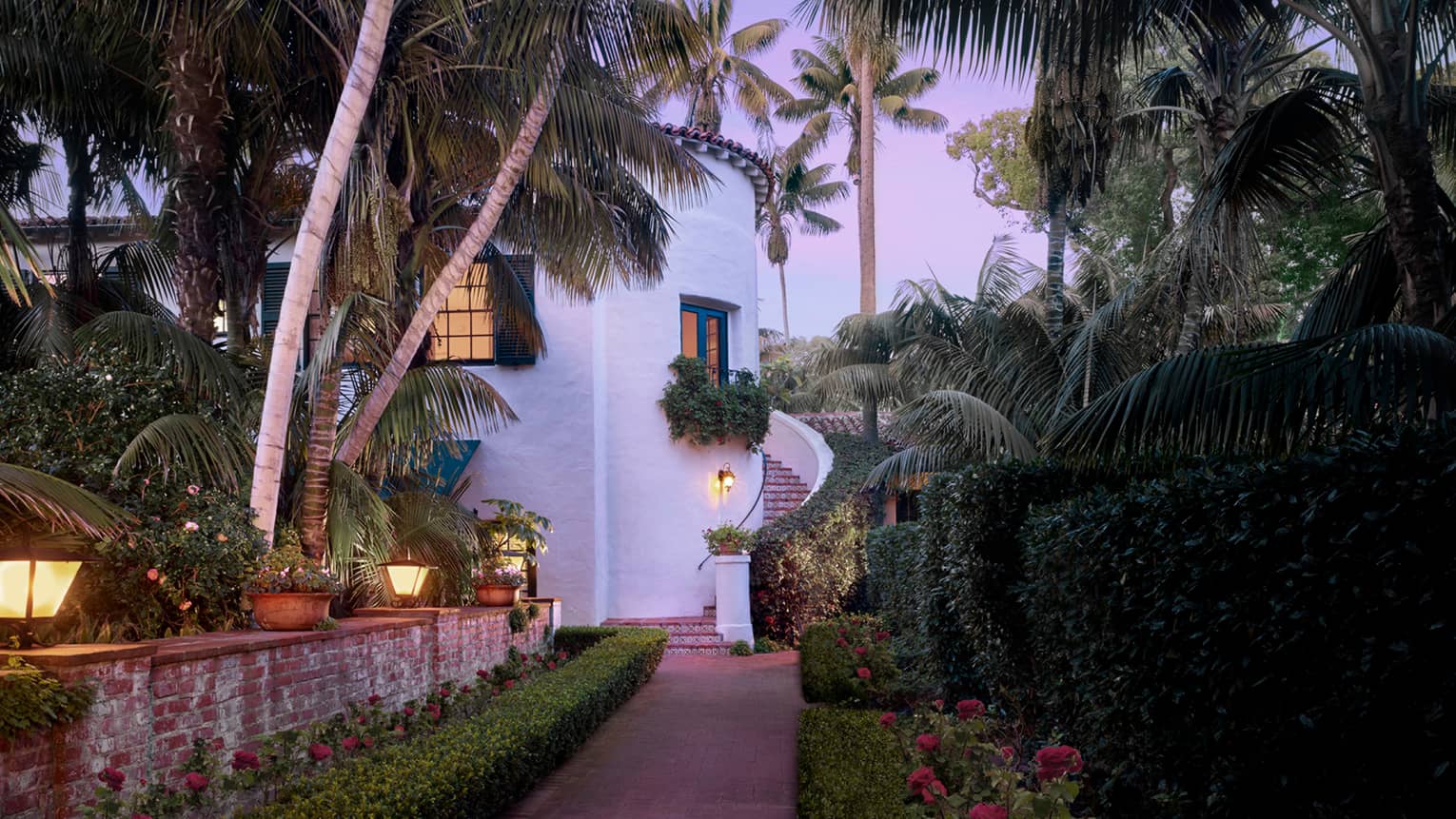 White concrete Honeymoon Suite with winding outdoor staircase by garden path under palms