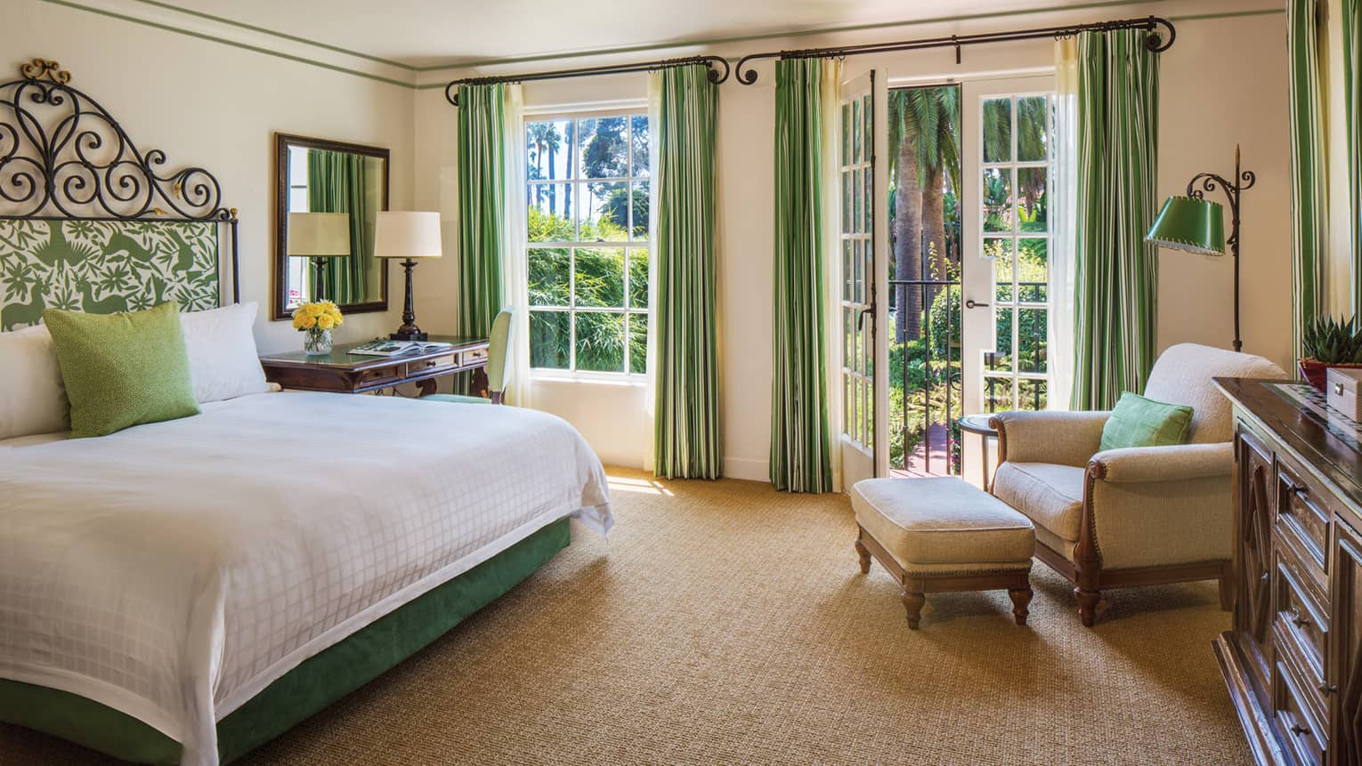 Bed with padded headboard by writing desk, double windows, corner armchair and ottoman