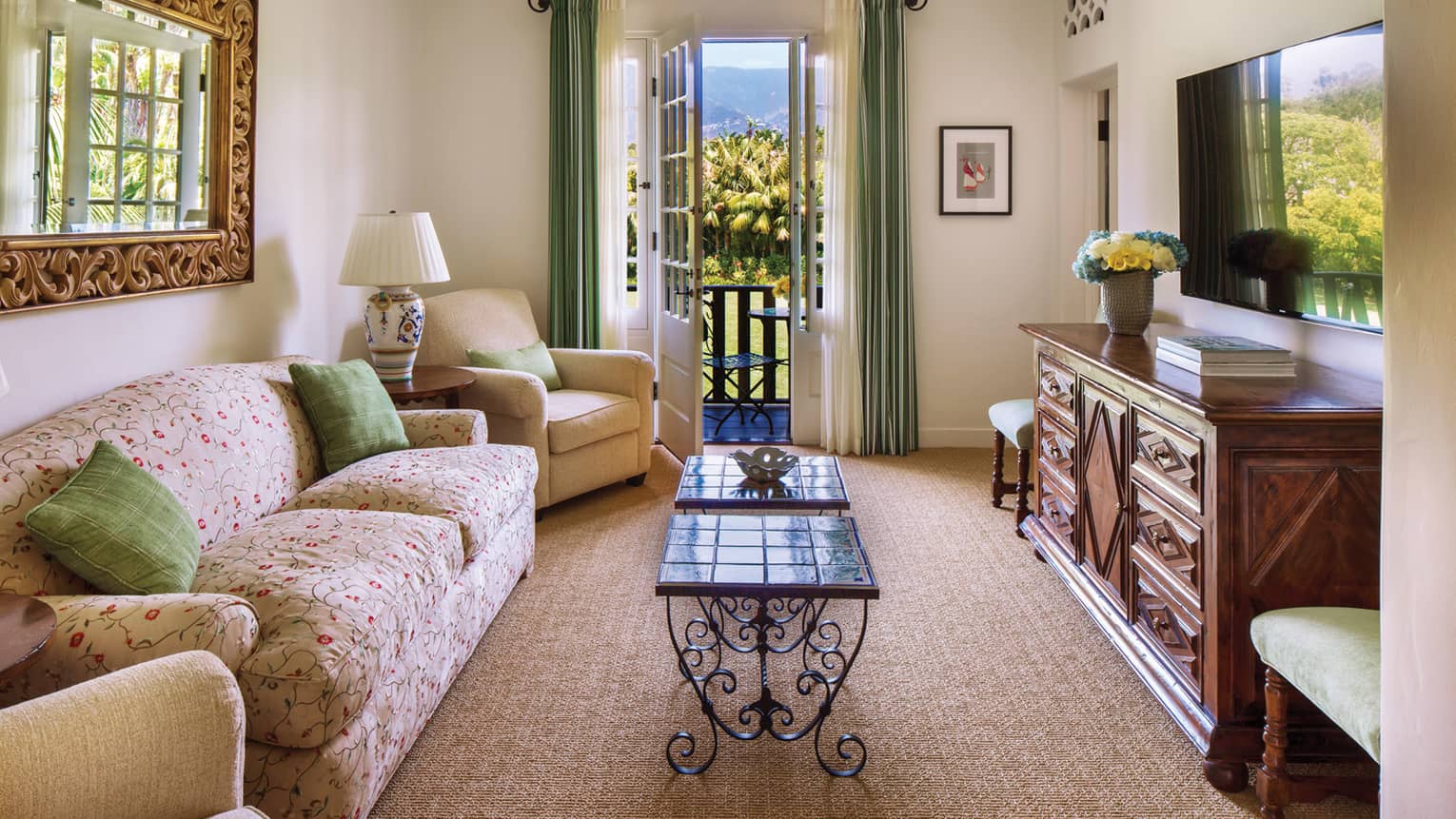 Floral loveseat with green accent pillows, across from wood dresser, open balcony door