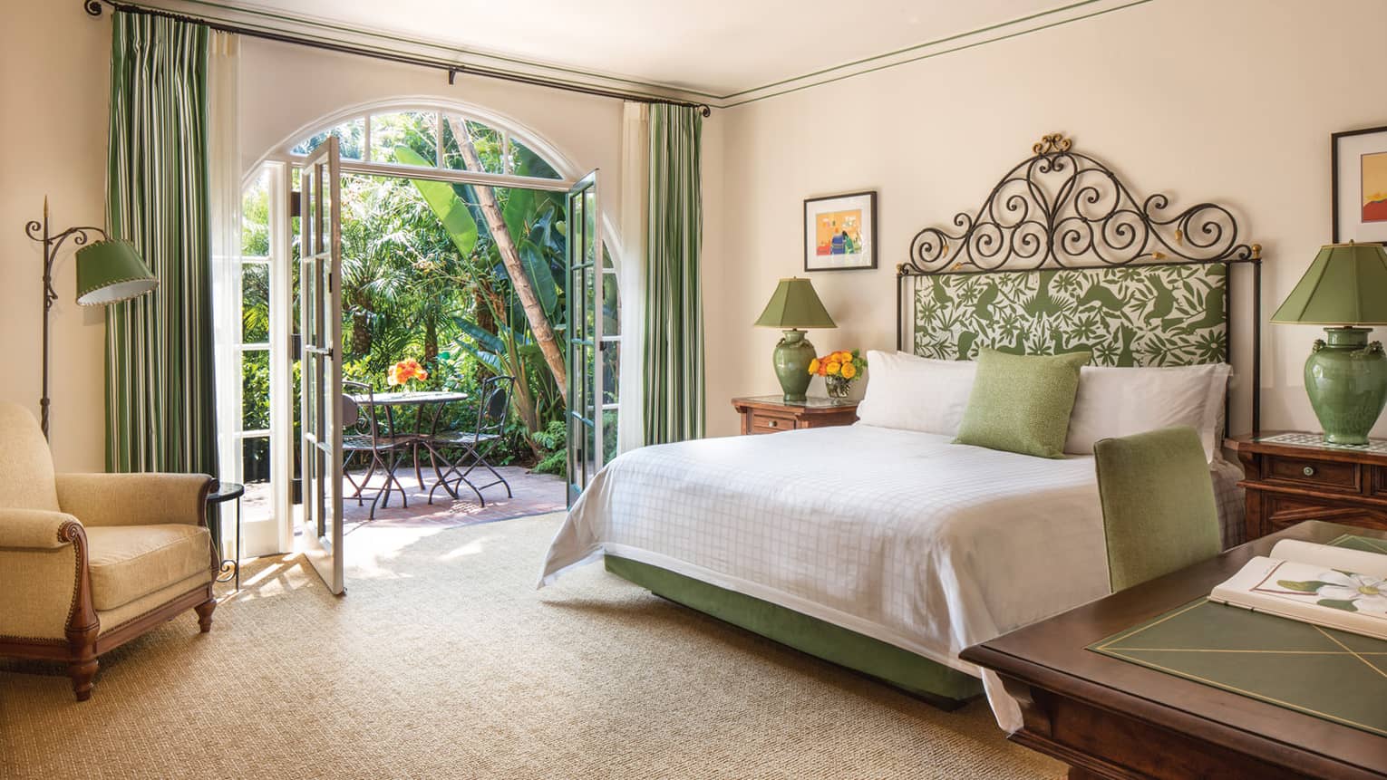 Open double French doors to patio, table by bed with iron headboard, green accents 