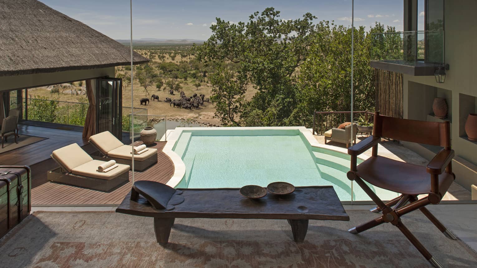 Several lounge chairs are set up surrounding a pool, all overlooking the horizon on the Serengeti