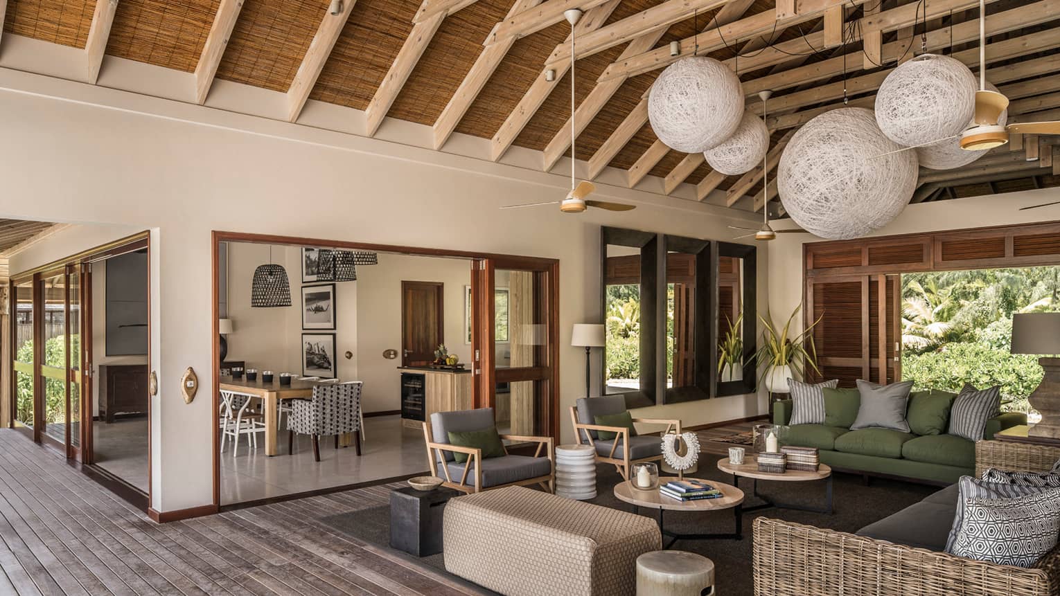 Large wicker globe chandeliers hang from beamed roof over open-air living room