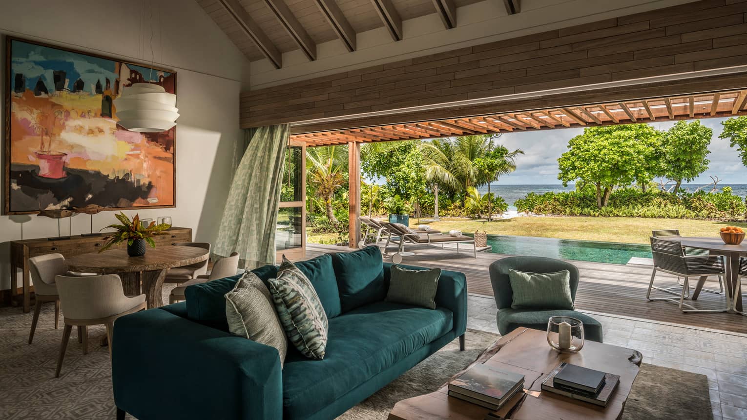 A blue couch sits in the middle of a sitting room overlooking a pool, with the ocean in the distance