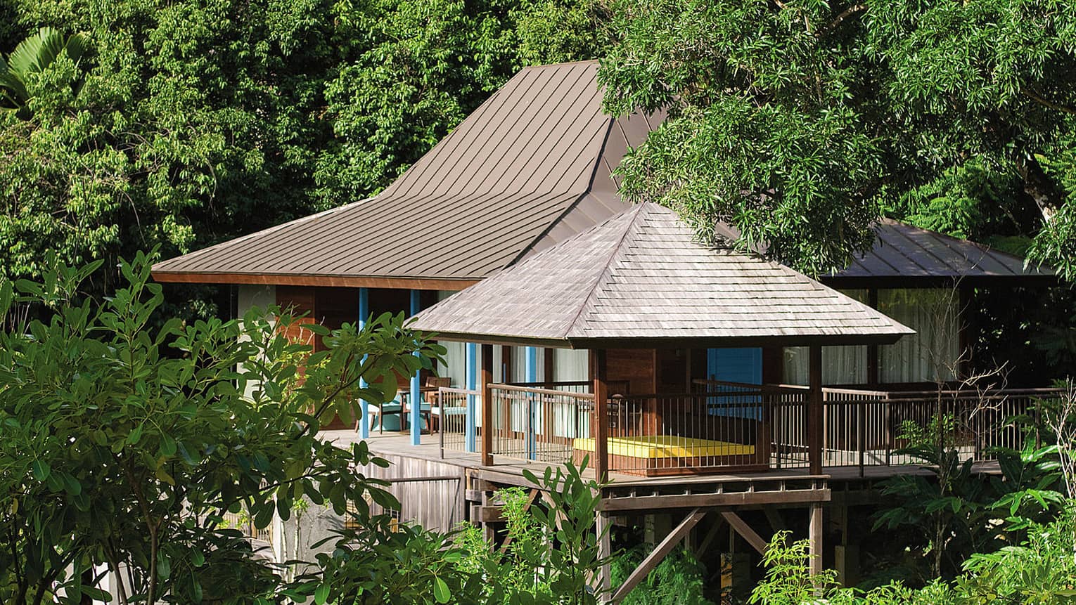 Exterior view of mountain villa with large patios, chairs surrounded by trees