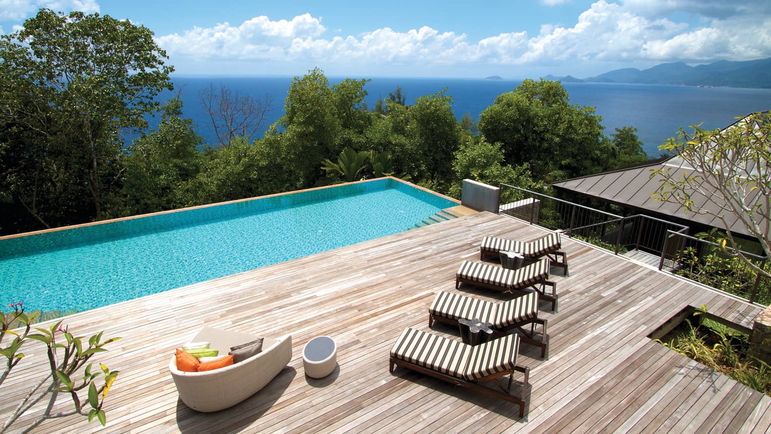 Looking over large deck with wood lounge chairs, sofa, plunge pool