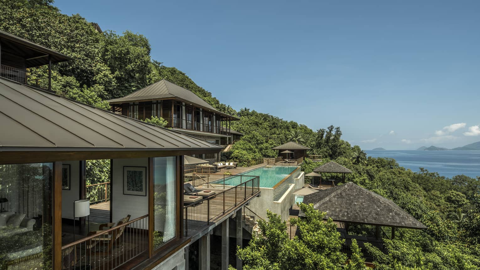 Four-Bedroom Residence Villa roofs, patios amid trees on mountain, ocean below