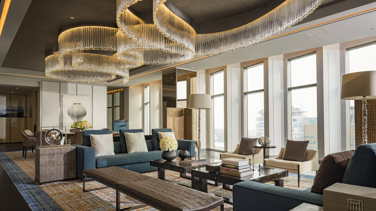 Presidential Suite seating area with large blue sofas, long leather bench, tables under modern chandeliers from soaring ceilings