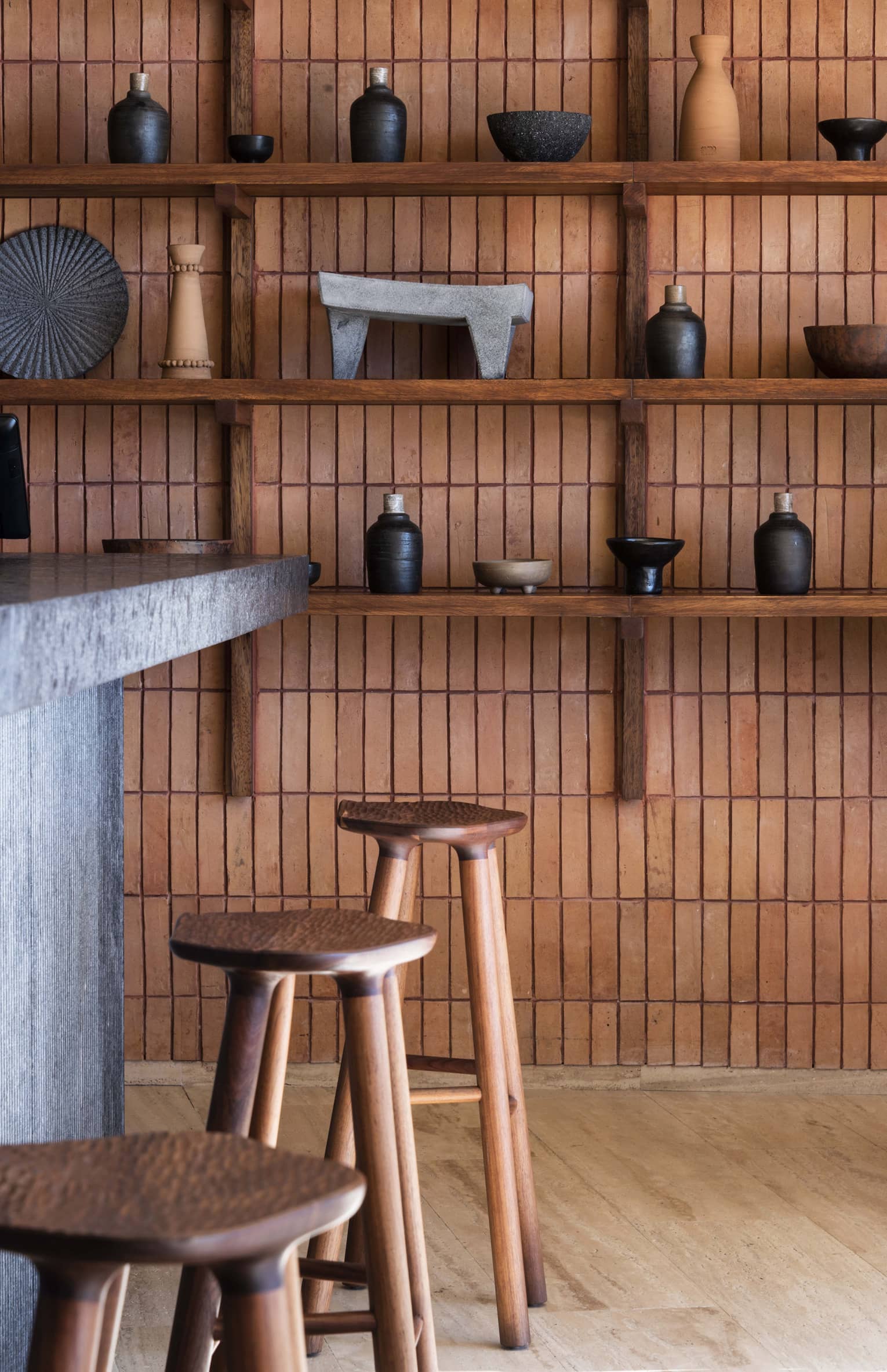 Close-up of wooden stools at a bar, and wooden shelves on a wall displaying Mexican handicrafts