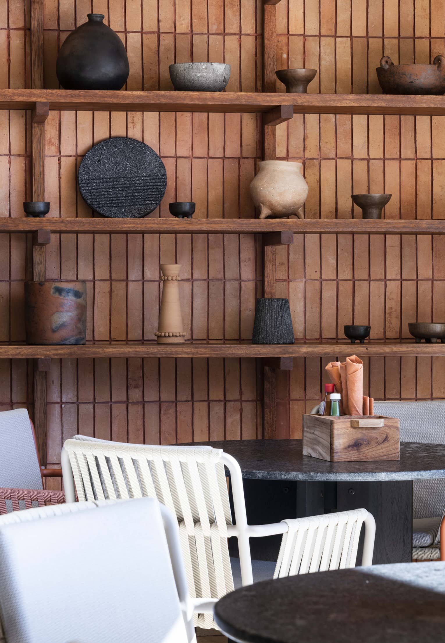 Tables and chairs in restaurant, and a wooden wall with wooden shelves displaying Mexican handicrafts