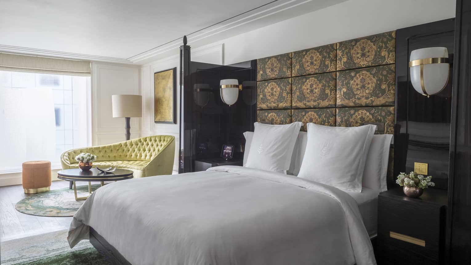 White bed against dark fabric-panelled wall with view of living area