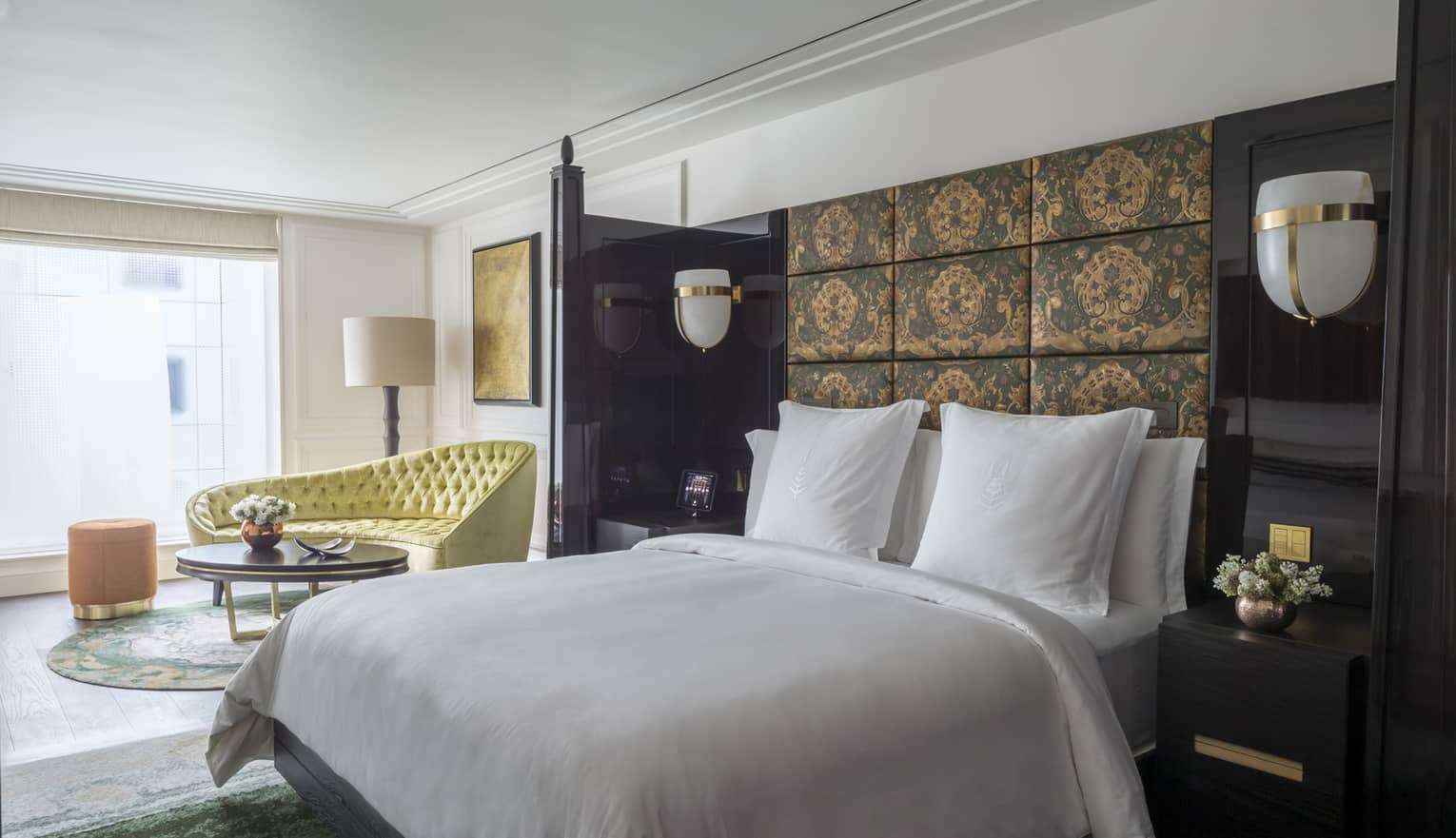 White bed against dark fabric-panelled wall with view of living area