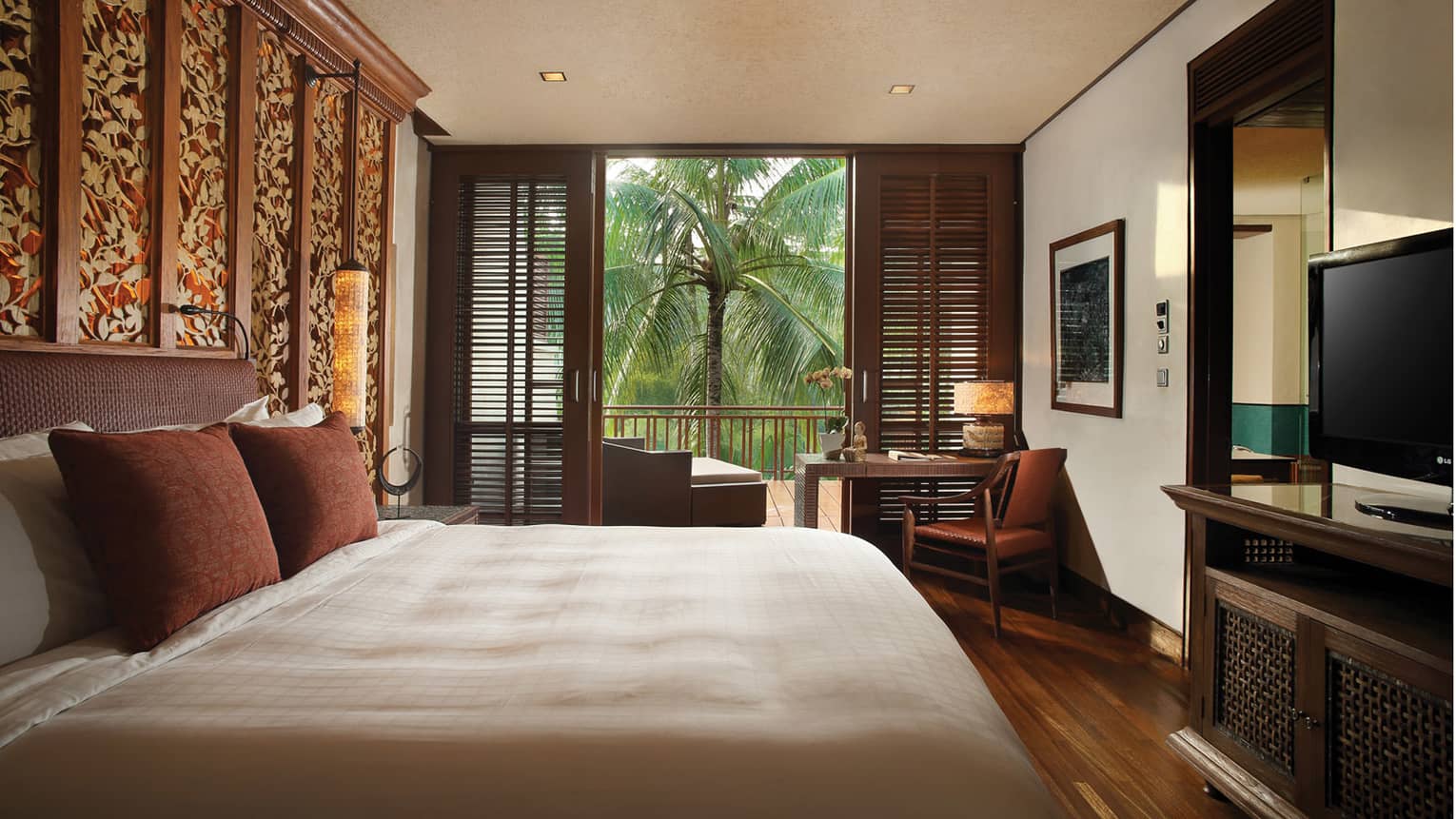 Family Suite bedroom with king-size bed, brown pillows, TV, wood shutters opening to patio with palm tree