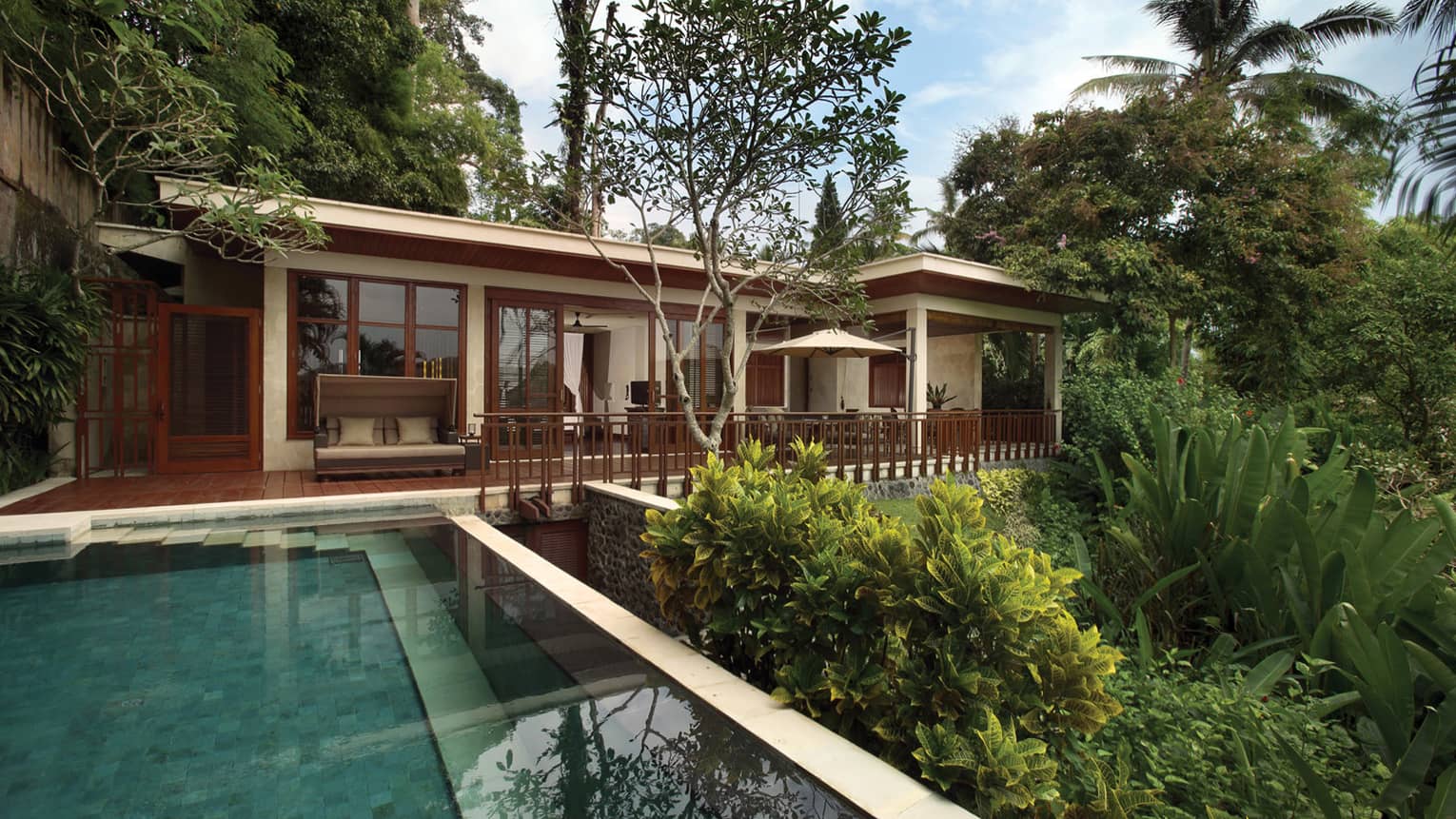 Exterior of Sayan Villa looking past pool and garden, up at deck and white bungalow with wood trim