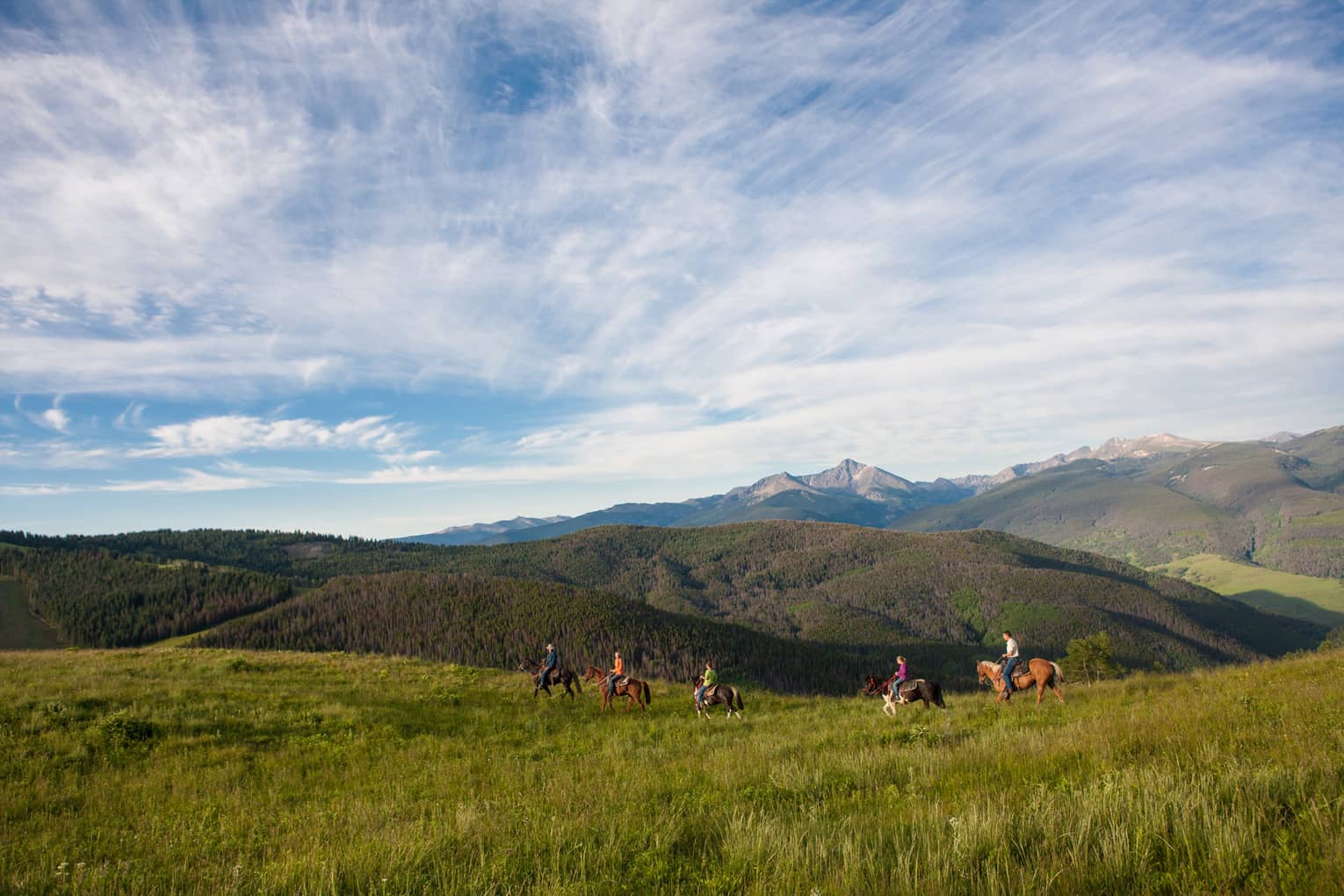 A group of people on horseback riding along grass and hills.