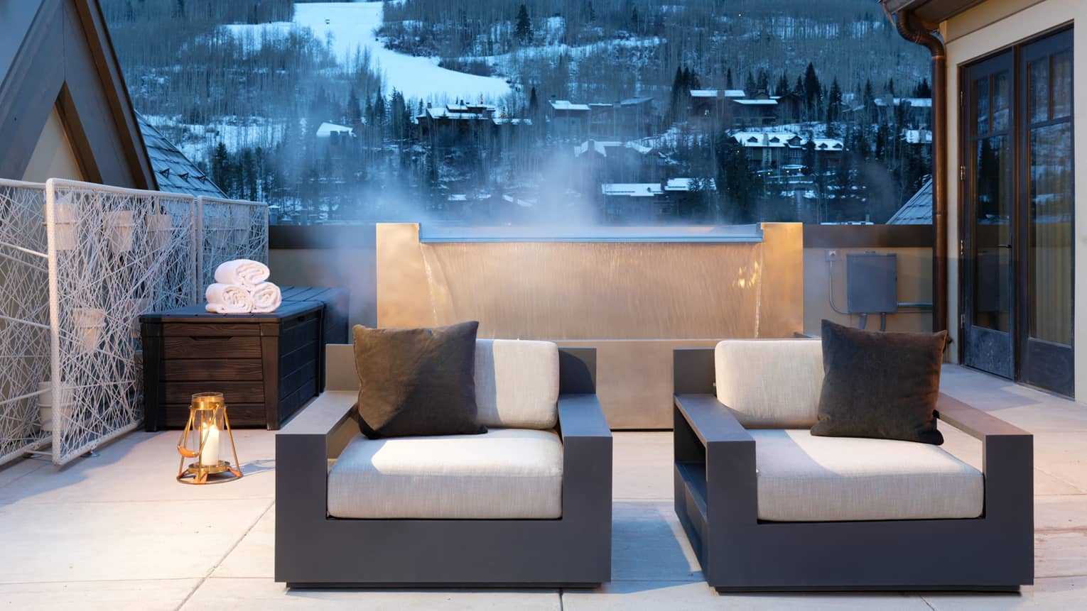 Plush patio armchairs in front of steaming fountain, snowy mountains in background