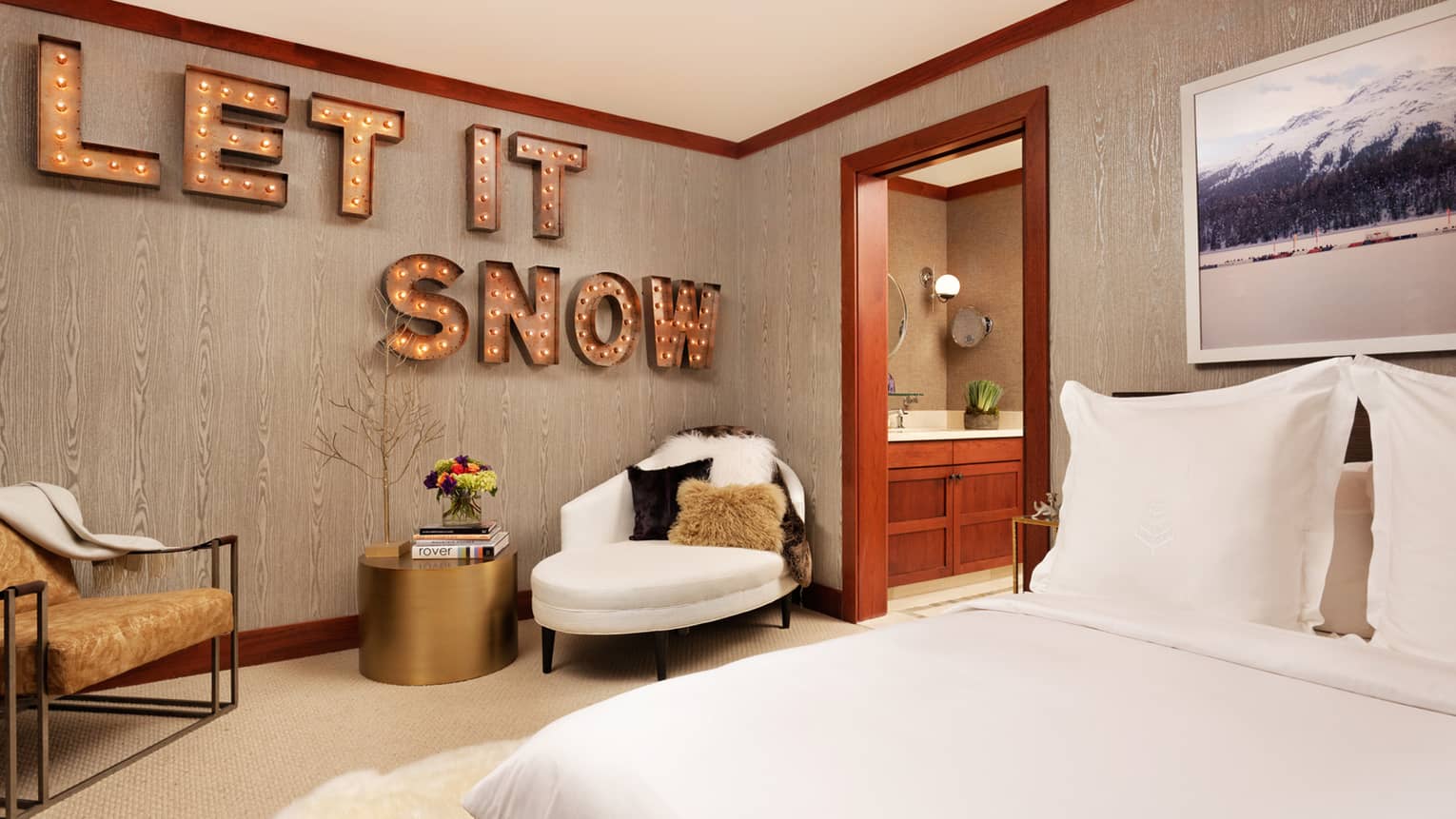Bed across from two armchairs, brass table, large sign with lights reading Let It Snow on wall
