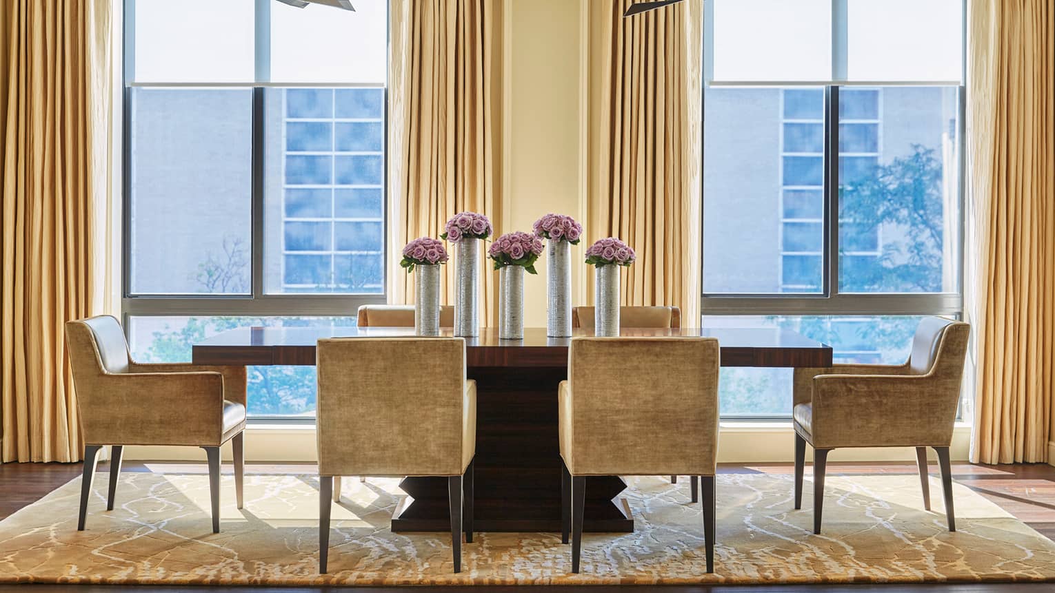 Imperial Suite modern dining table with golden brown velvet dining chairs around long wood table with tall silver vases, purple flowers