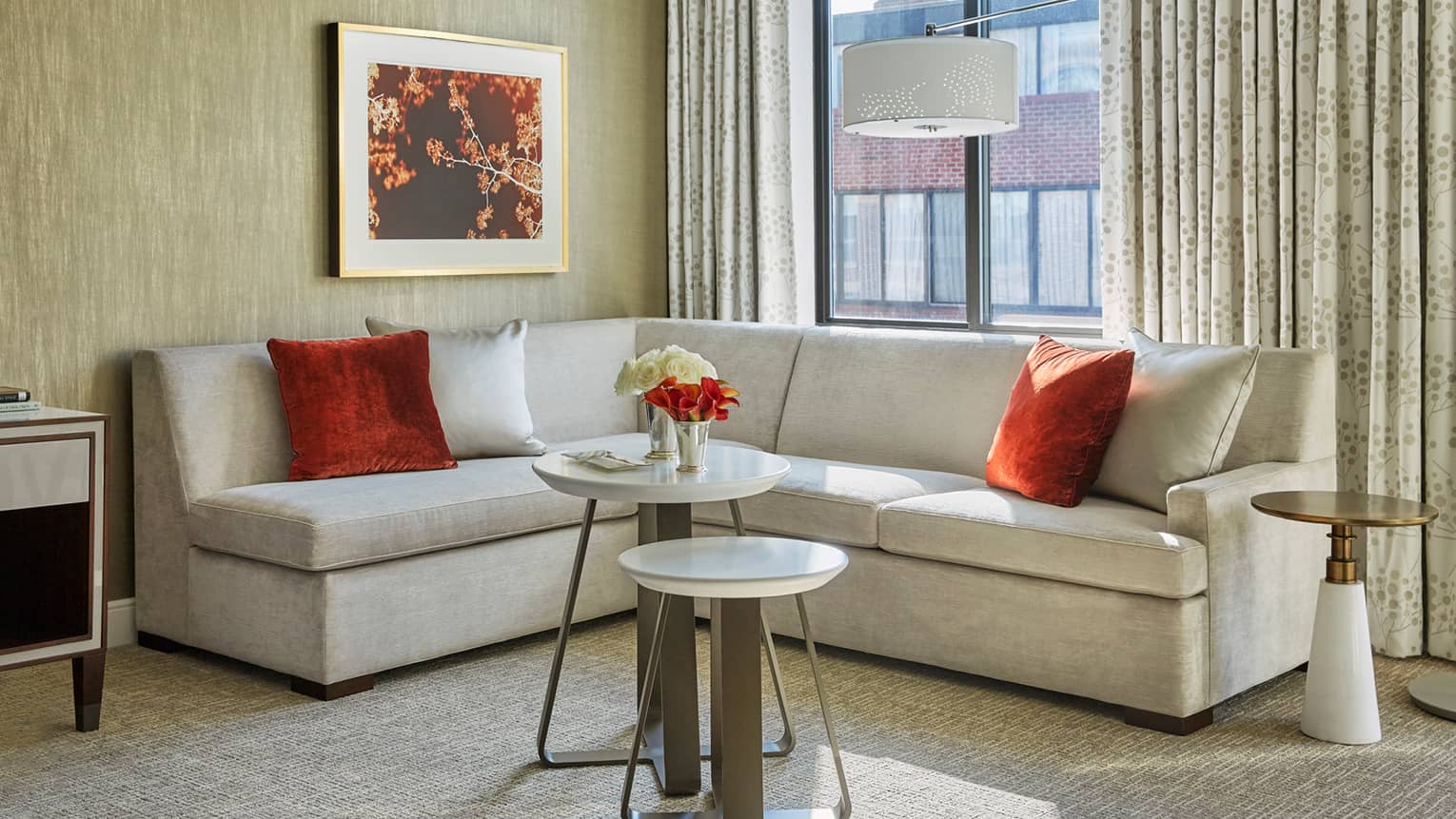 Grey L-shaped velvet sofa with red, silver accent pillows in corner of room