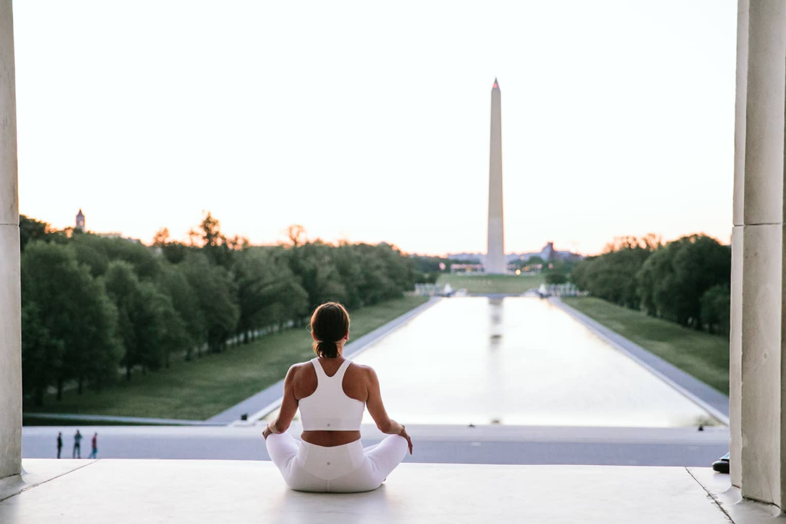 A woman in workout clothes is sitting and looking at the Washington Monument.