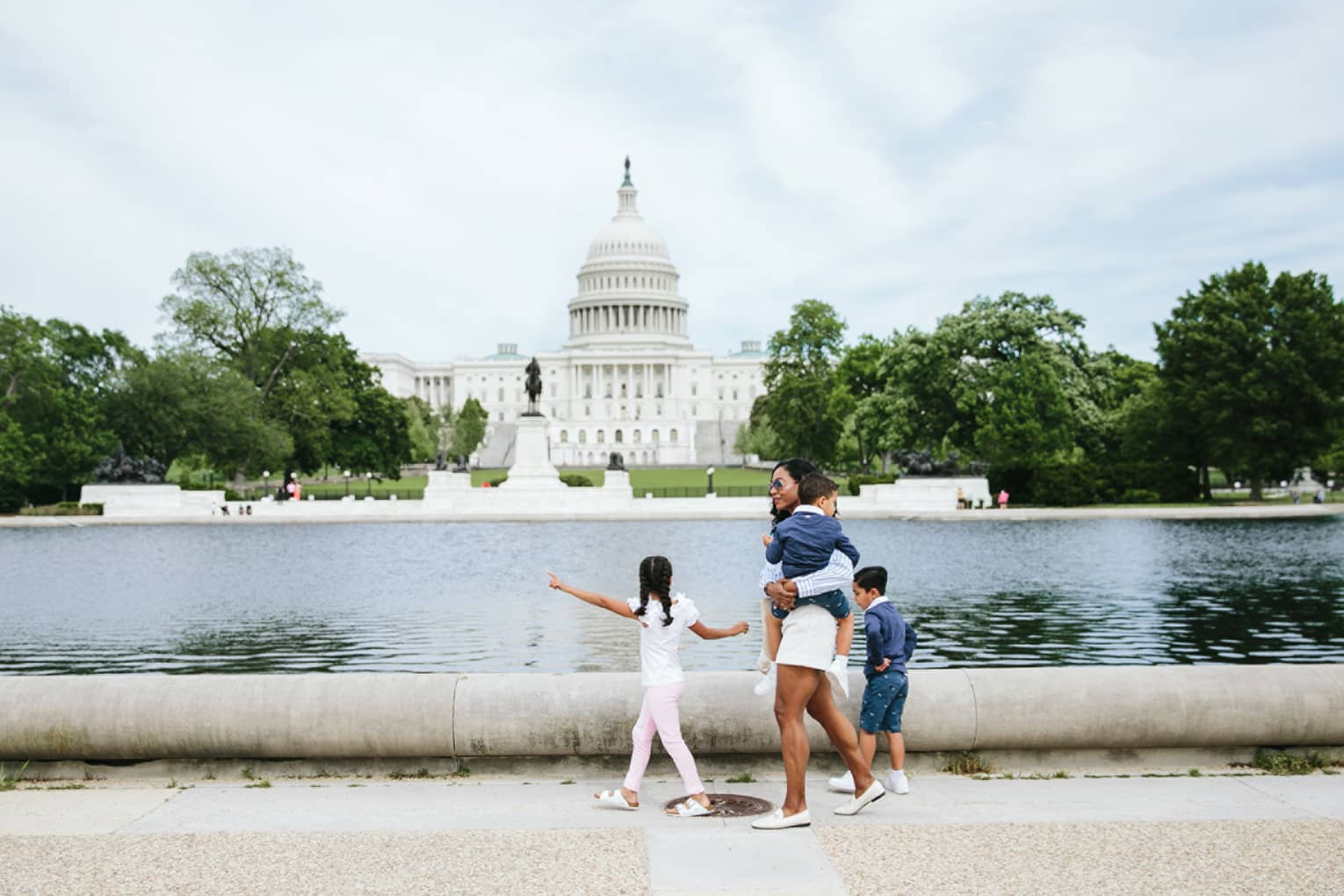 Woman and three children walk in front of the Capitol reflecting pool in Washington, DC, with Capitol building in background