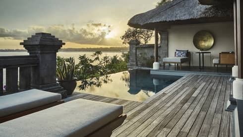 Ocean sunset reflecting on private villa swimming pool, palm trees, thatched roof, lounge chairs