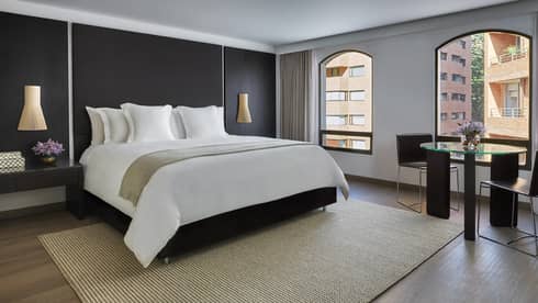 Grand Premier Room black wall, bed with white linens, bamboo rug, sunny windows with street views