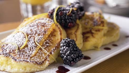 Close-up of fluffy pancakes topped with icing sugar, blackberries and citrus peels