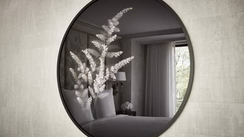 Hotel room bed, window reflected through round mirror with floral accent