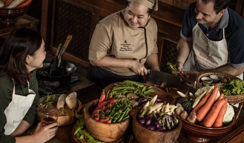 Chef chops mushrooms in front of couple, bamboo baskets with vegetables