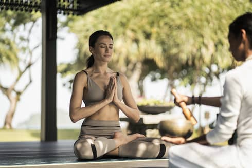 A woman sitting outside doing a yoga breathing pose.