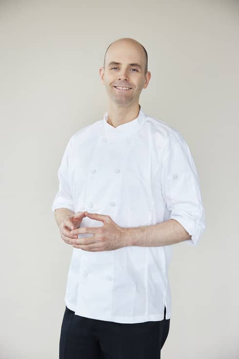 A smiling Pastry Chef Patrick Thibaud stands with steepled fingers