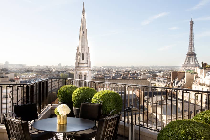 Patio dining table with white roses, potted shrubs iron balcony overlooking Paris rooftops, cathedrals